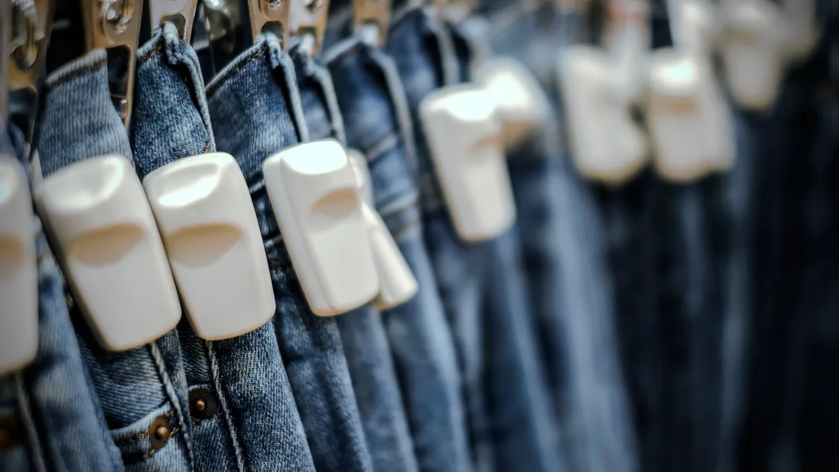 A rack of denim jeans with white store tags clipped to them.