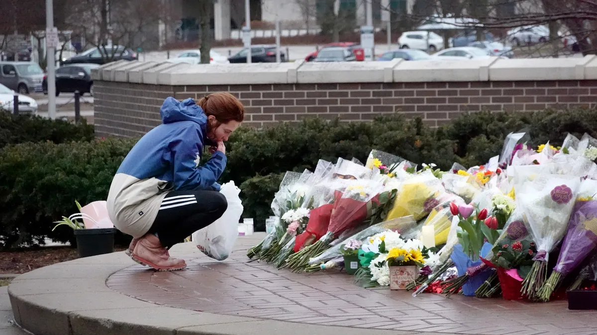 A young woman dressed warmly crouches down to add flowers to a pile of dozens of bouquets.