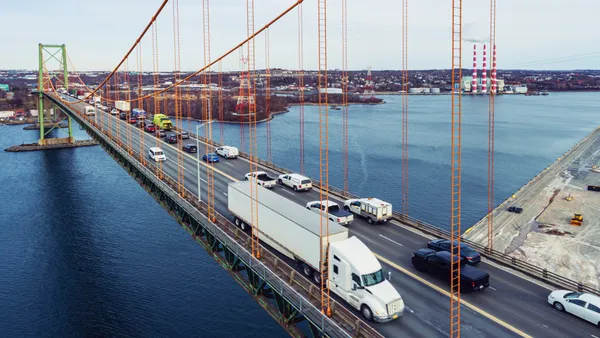 Aerial drone view of a tractor-trailer crossing a suspension bridge with heavy passenger traffic in the opposite lane.