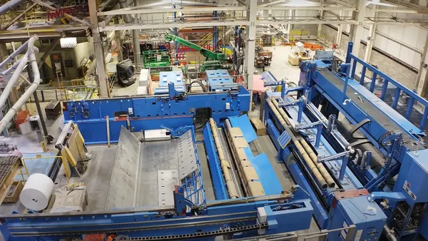 A large roll of white paper is next to industrial equipment in a manufacturing facility.