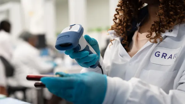 A Grail employee in white coat and blue gloves works with a blood sample.