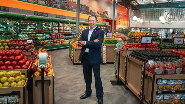 Man standing in a suit with arms crossed in a grocery store produce section