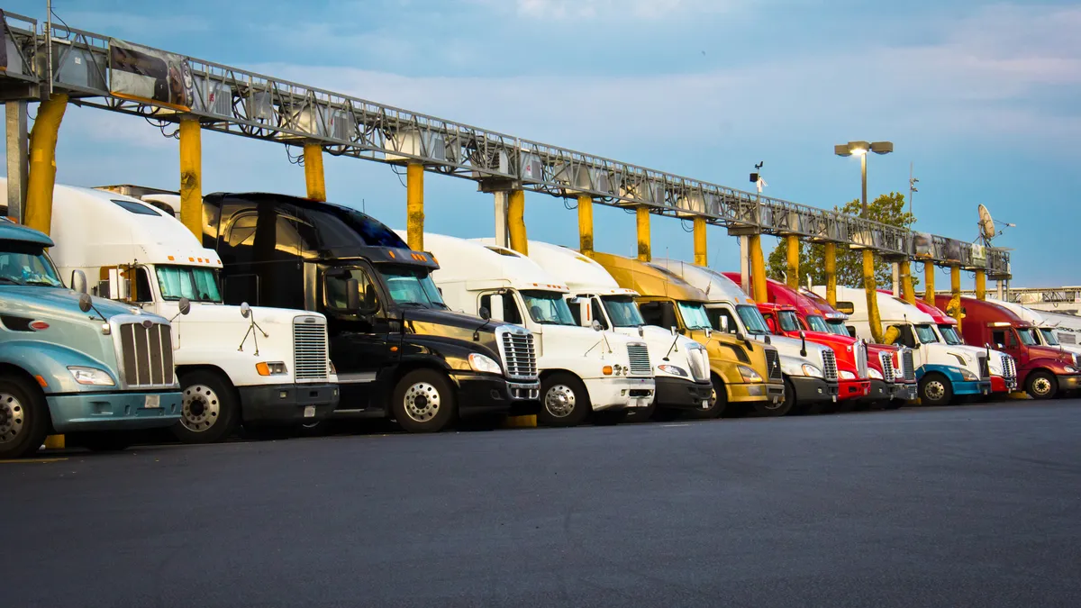 Several diesel semi-trucks lined up for fueling at a truck stop blue sky white clouds.