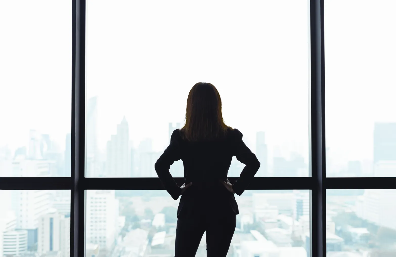 Business person standing in front of window looking at city view.