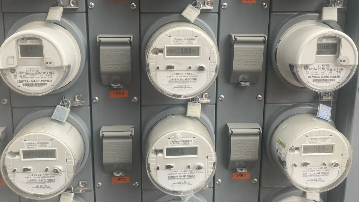 A wall of six electric smart meters against gray, metal paneling.