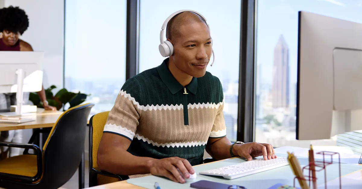 A professional wearing headphones works at a computer in an office.