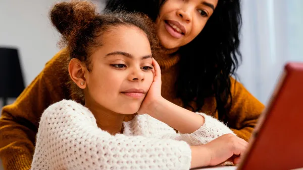 Smiling teenager helping younger sibling during online school with tablet