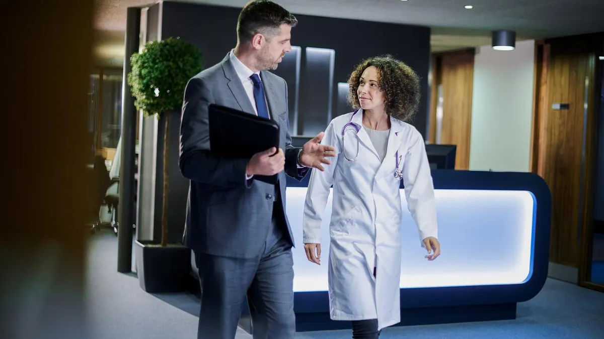 Female physician in lab coat walking with business man.