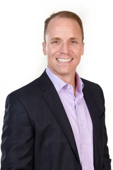 A person wearing a dark suit jacket and light colored shirt smiles for a photo.