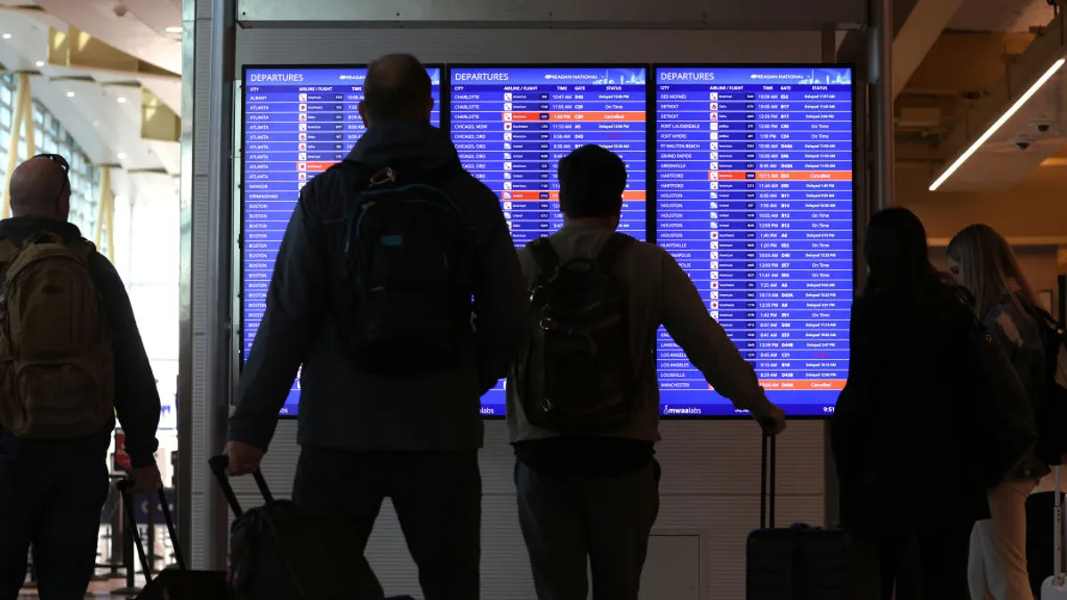 Passengers gathered around an airport screen showing canceled flights