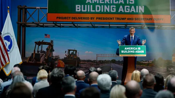 Man in blue suit standing at a podium with sign reading "America is building again" with a large audience watching.