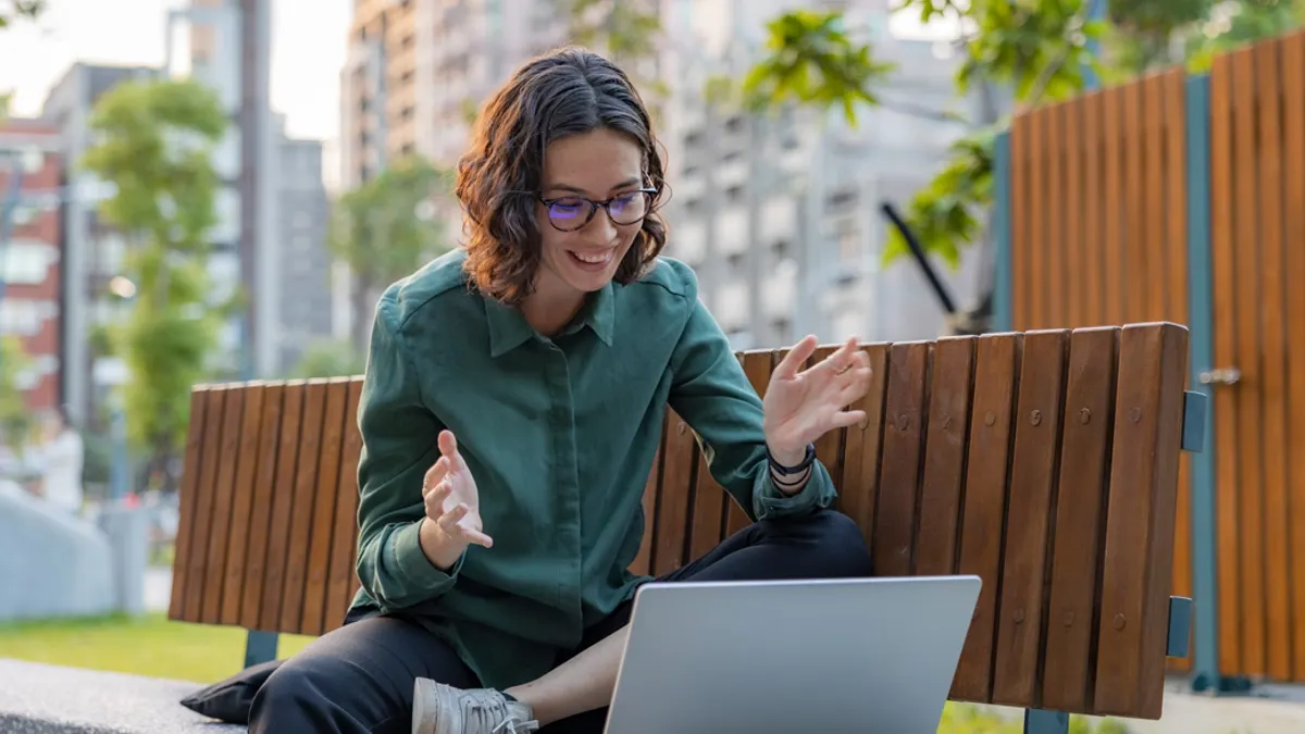 Young woman smiling and doing remote work video call at park bench