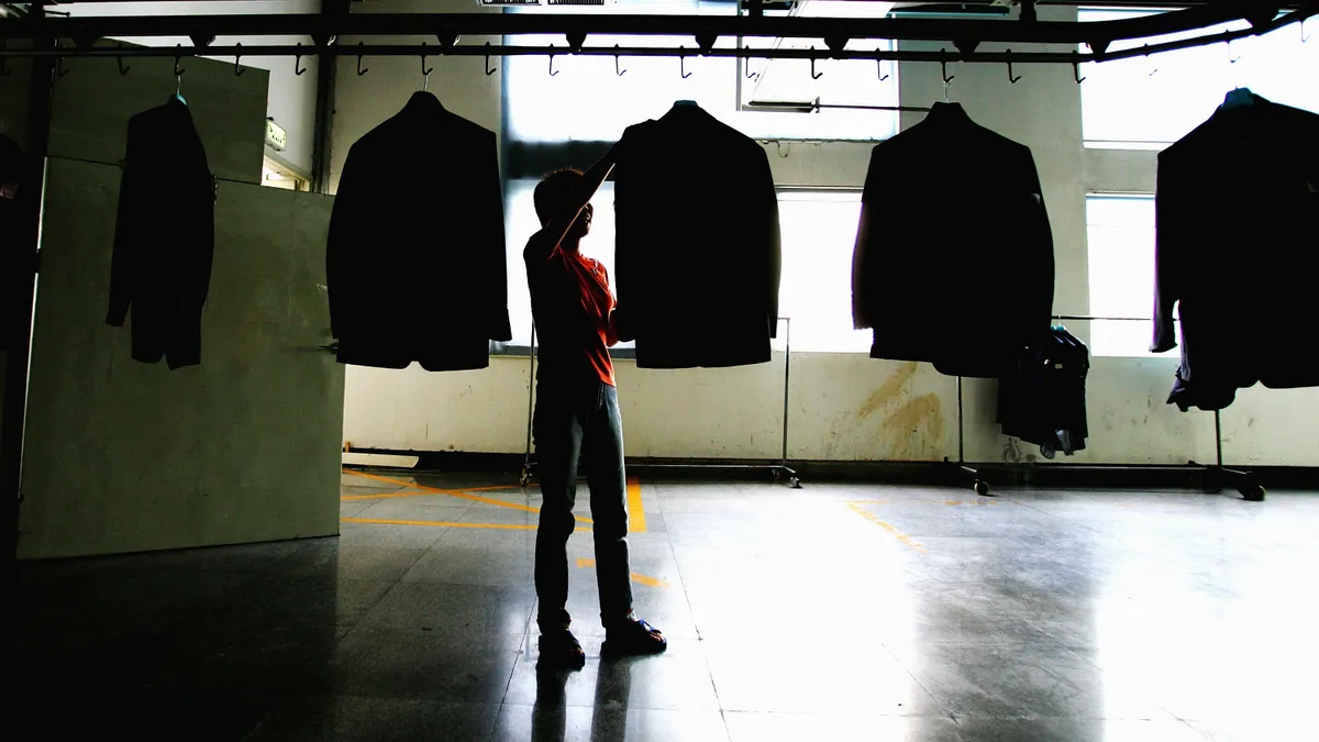 A laborer stands on a factory floor checking suit jackets on hangers at the Youngor Group textile factory in Ningbo, Zhejiang Province, China.