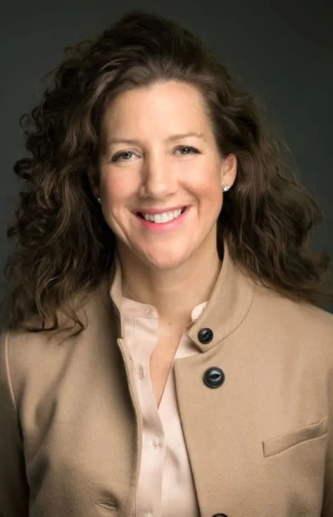 An image of a woman with wavy hair wearing a tan coat.