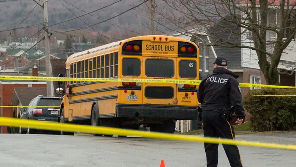 A police officer and a school bus surrounded by yellow tape