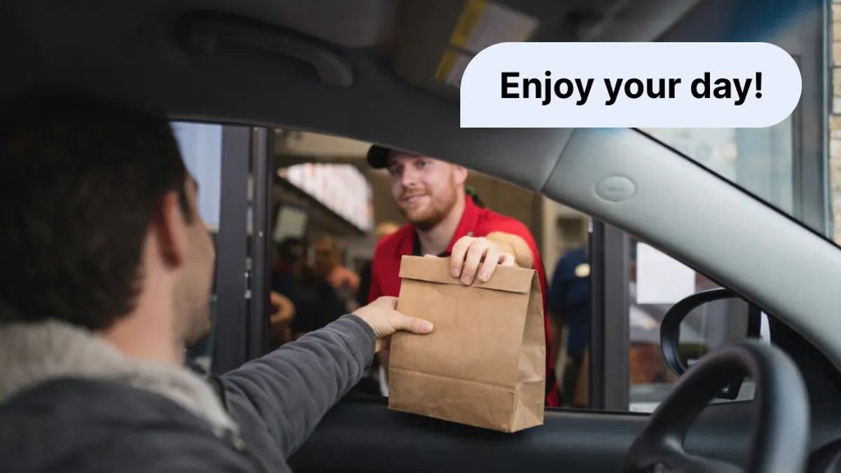 A photograph of a fast food employee handing a paper bag to a person in a car.