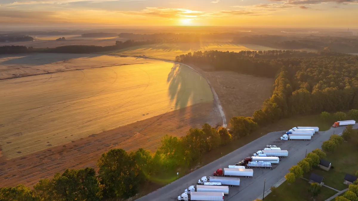 Big parking truck stop for tractor trailers rest area near busy with fields and sun in background.