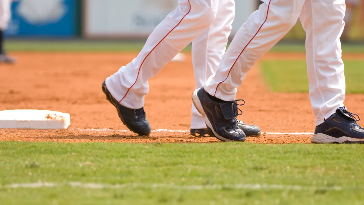 A pair of baseball players walks past third base on the infield, with another player and second base in the background.