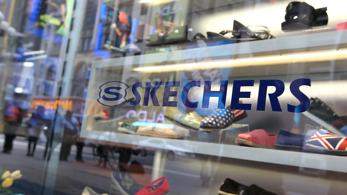 The Skechers logo is pictured on a storefront window, which shows shoes on display inside.