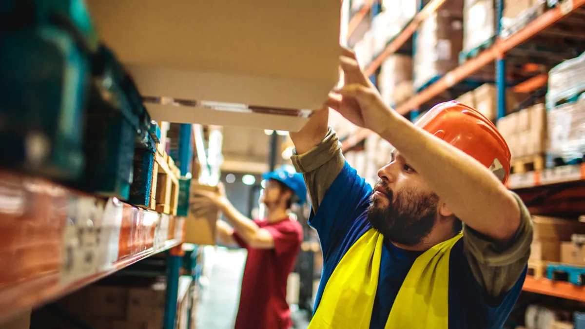 Person in hardhat pushing box on warehouse shelf