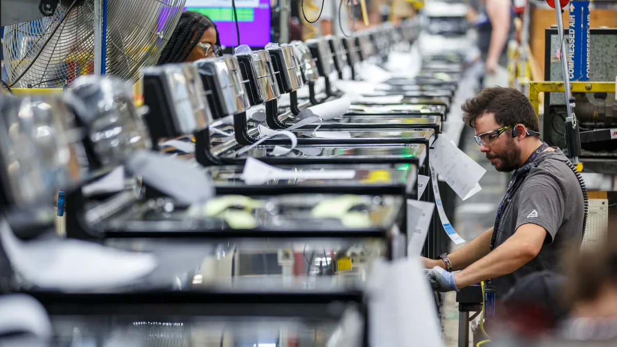 A person wearing goggles works on a line of household appliances in an industrial setting.