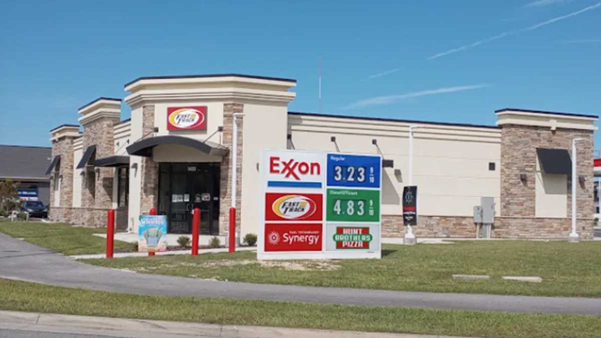 A photo fo the exterior of a convenience store. A sign over the door says "fast track" while a sign in front of the building says Exxon, Fast TRack and Hunt Brothers Pizza.