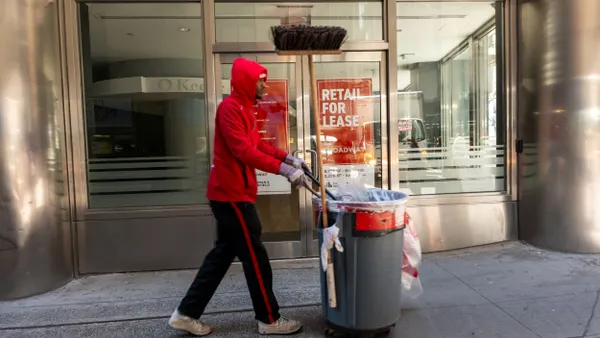 An individual pushes cleaning supplies down a city sidewalk.