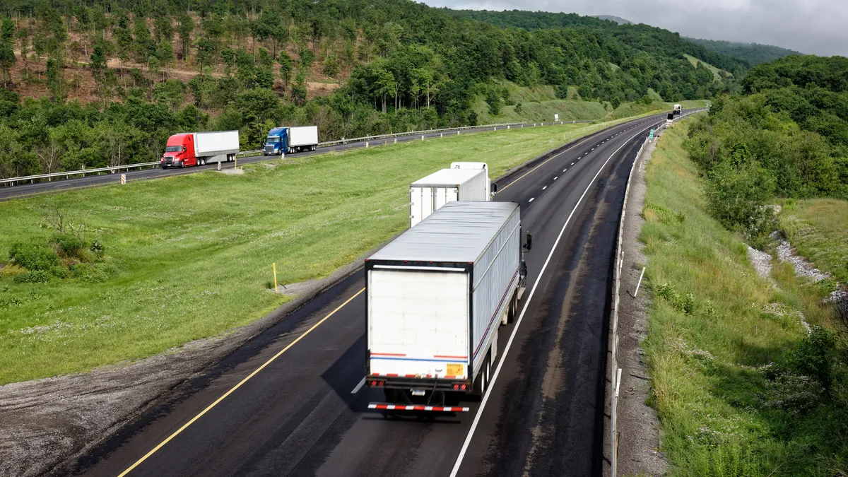 Trucks moving down an interstate highway through the scenic mountains filled with green trees.