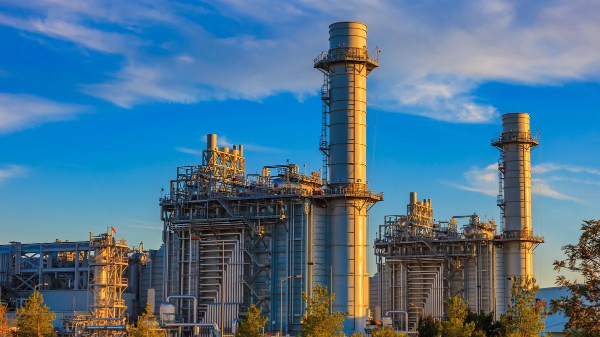 Natural gas fired turbine power plant with it's cooling towers rising into a cloud filled blue sky.