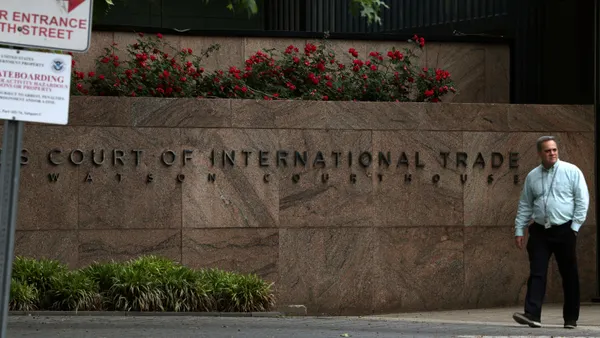 A person walks near a wall that has lettering that reads: "Court of International Trade Watson Courthouse."
