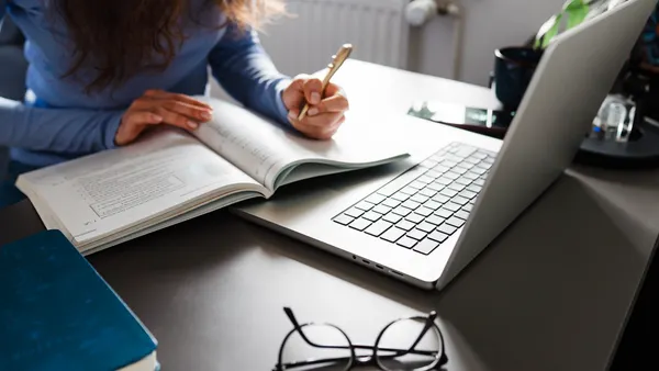 Woman Studying With Laptop And Open Book At Desk
