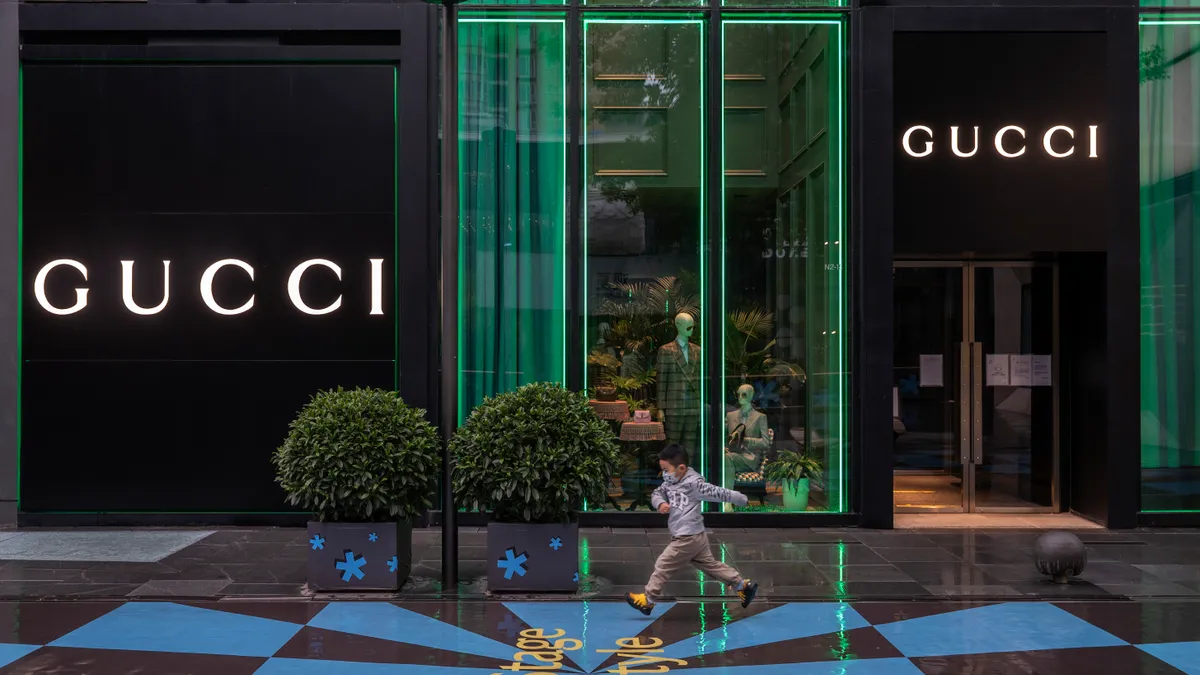 A small boy in a facemask runs by a closed Gucci store.