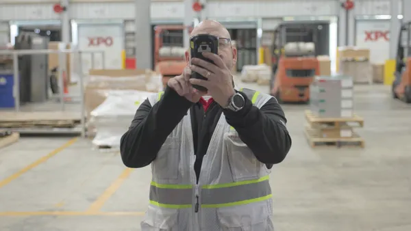 An XPO senior quality manager inside a facility holds a company-issued handheld device to photograph a trailer.