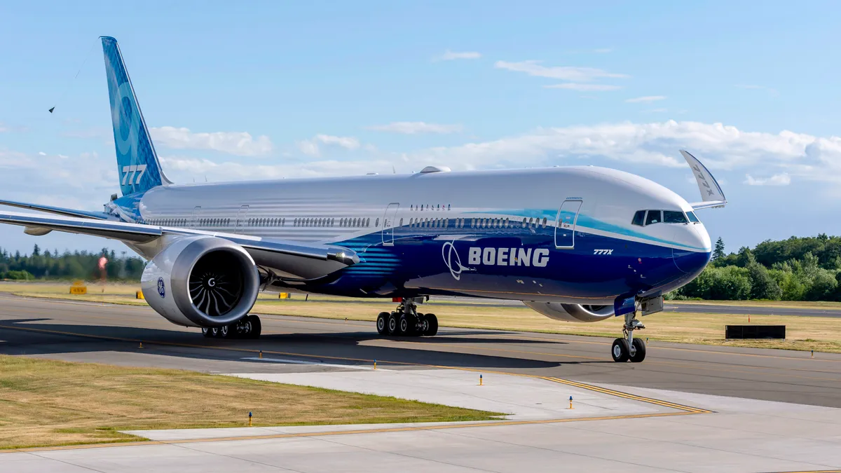 A white and blue 777x aircraft with the white Boeing logo on the runway.