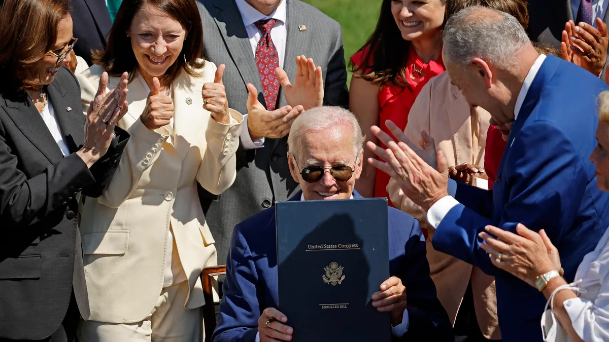 A crowd breaks into applause as President Joe Biden holds up a signed piece of legislation