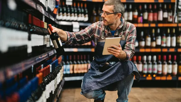 A person squatting in front of shelves of wine bottles.