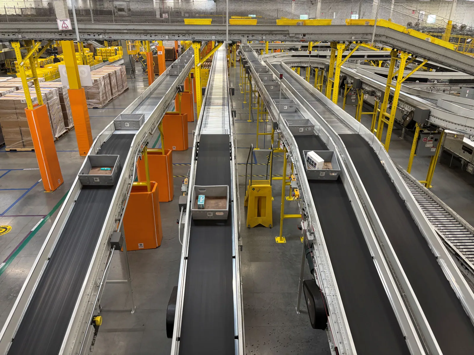 Gray trays with items are being transported on conveyor belts in a warehouse.