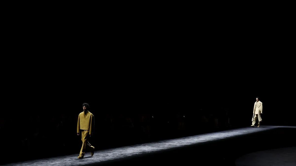 Models walk down an empty runway as seen from afar.