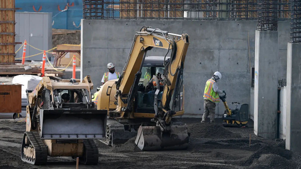 A group of construction workers labor around heavy equipment and vehicles.