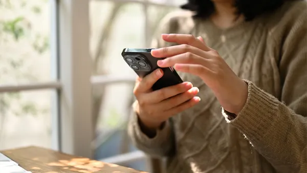 A person in a cozy sweater uses a smartphone near a bright window. The scene is warm and calm, with soft natural light enhancing a peaceful mood.