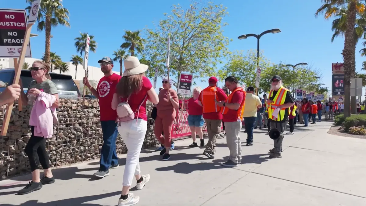 People walking on a sidewalk hold picket signs.