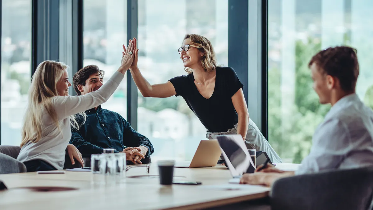 Female professional giving a high five to her colleague in conference room. Group of colleagues celebrating success in a meeting..