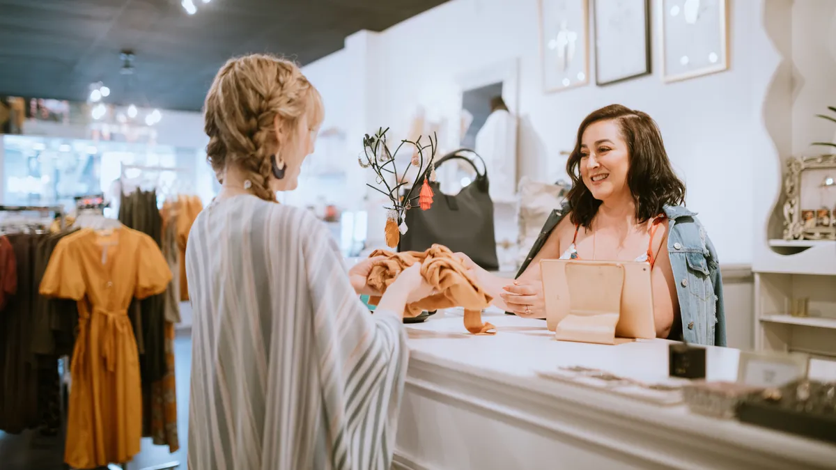 A fashionable Hispanic woman works in her small retail clothing store, selling new fashion items. She cashes out a customer.