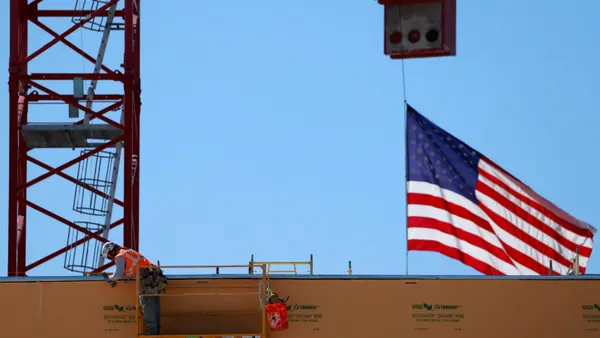 A construction worker on a jobsite crane near an American flag.