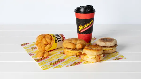 A photo of a breakfast combo meal including a cup, three breakfast sandwiches and a container of hash browns on a wrapping paper that says "Rutter's" on a white background.