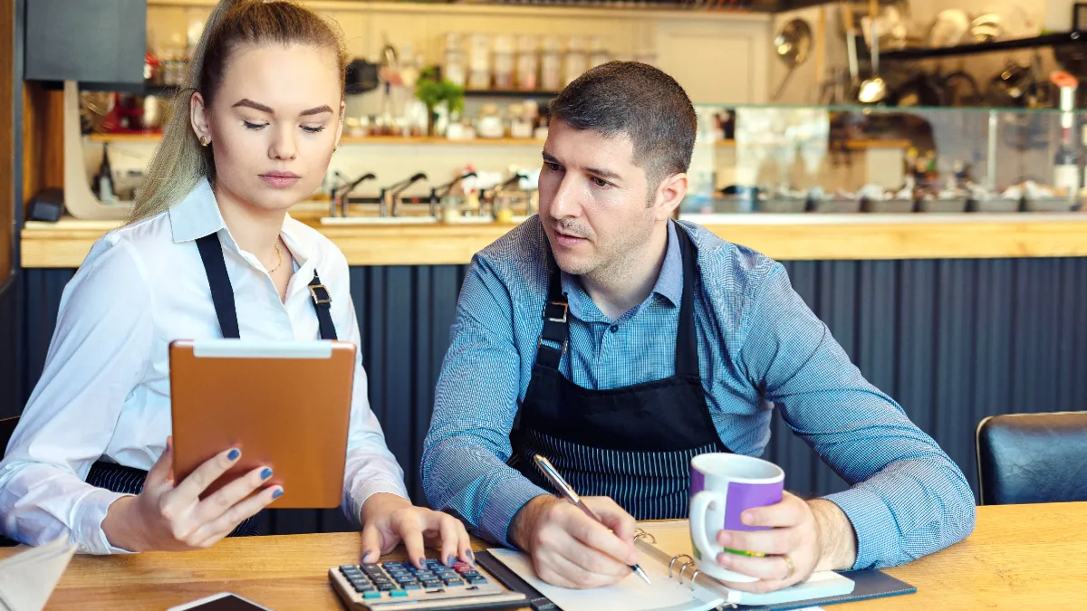 An image of a man and a woman looking at a tablet and doing financials in a restaurant.