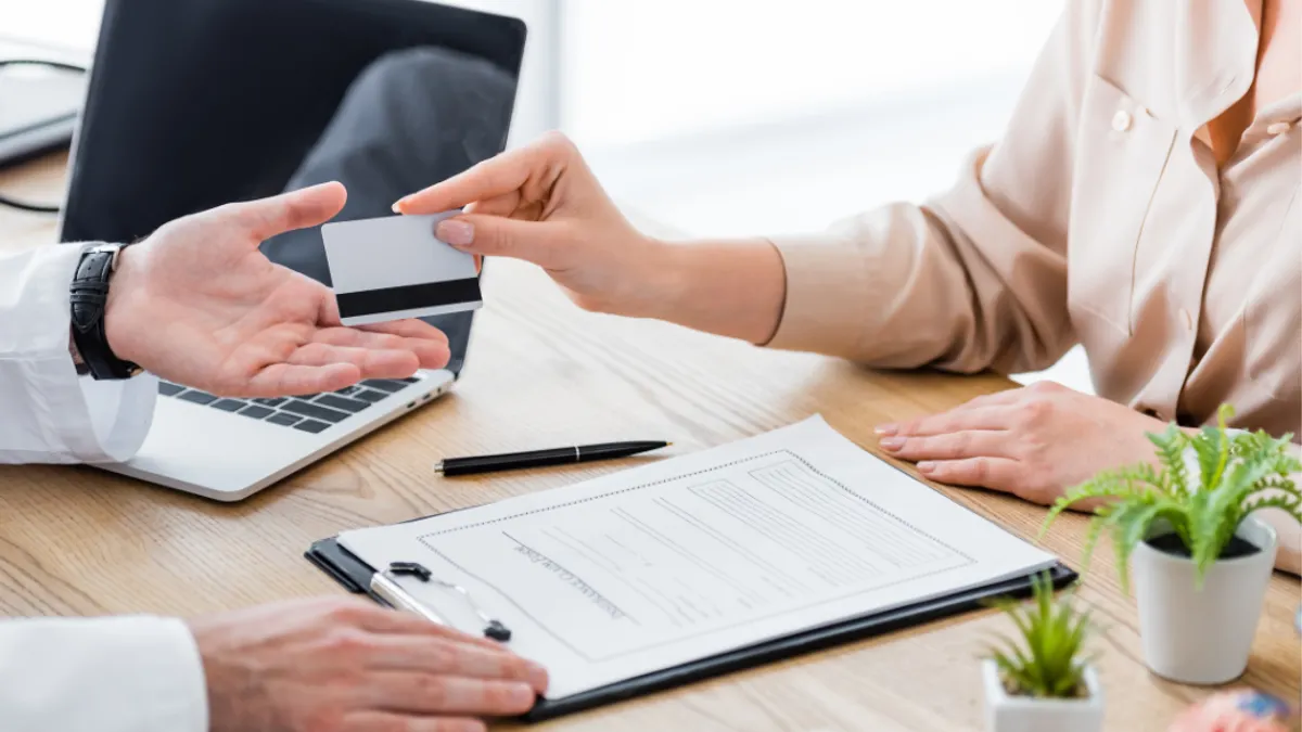 Cropped view of patient at table with insurance claim form giving credit card to doctor.