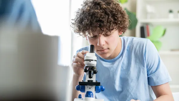 A teenage boy looks into a microscope in a biology class.