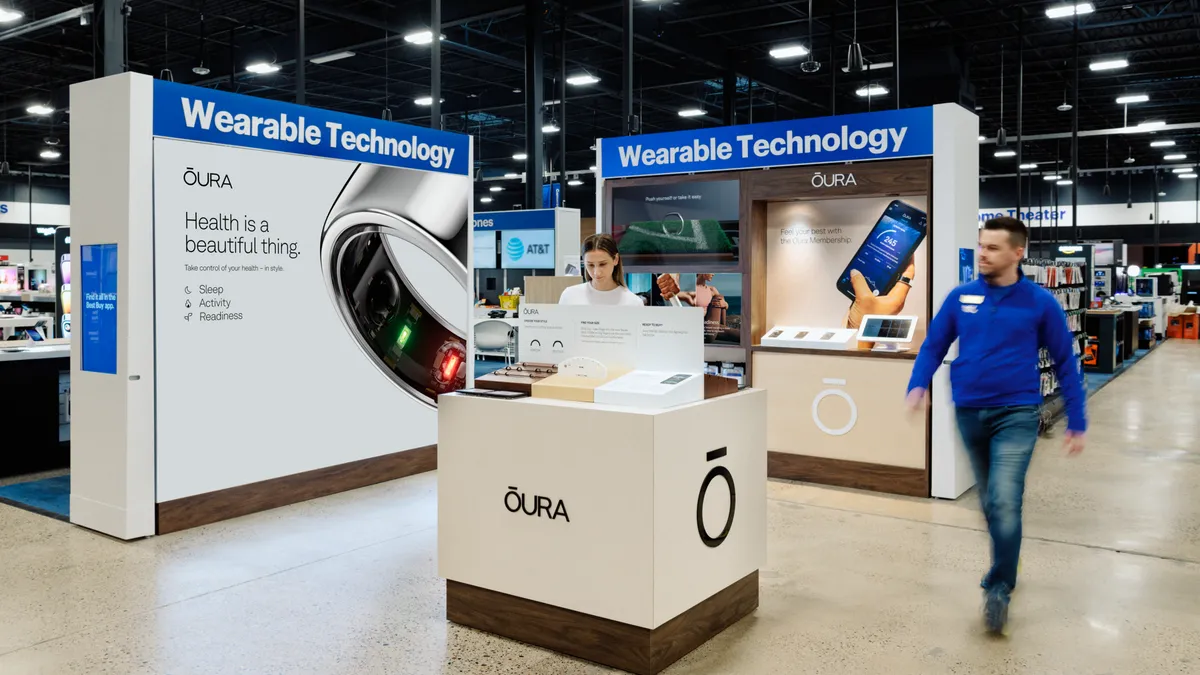 A person walks past a white store display with the Oura logo on it