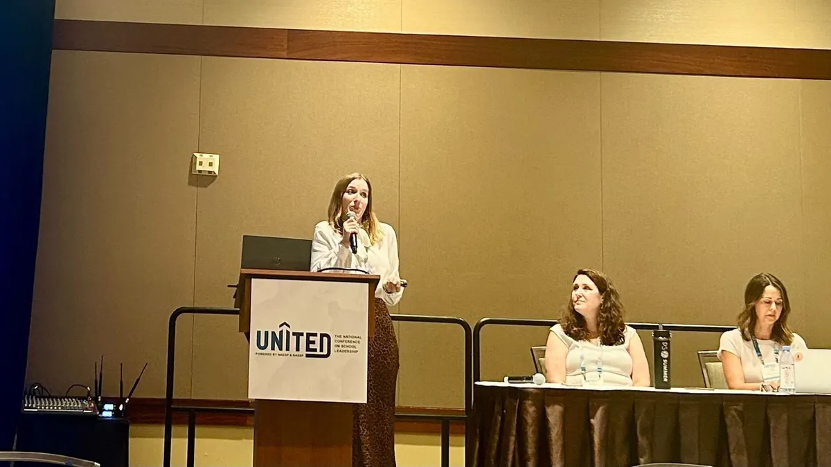 A district administrator stands at a podium that says "UNITED" while presenting on high-impact tutoring.